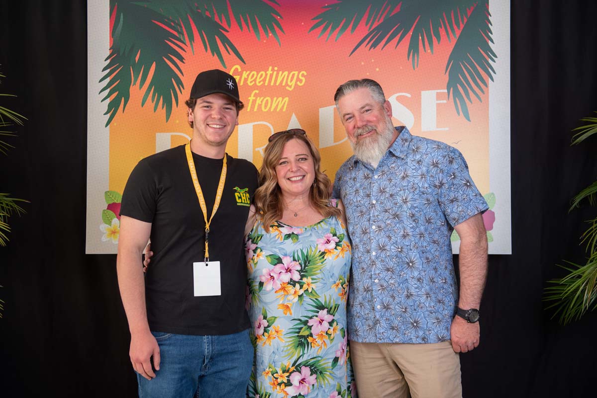 Three people in front of Greetings from Paradise sign