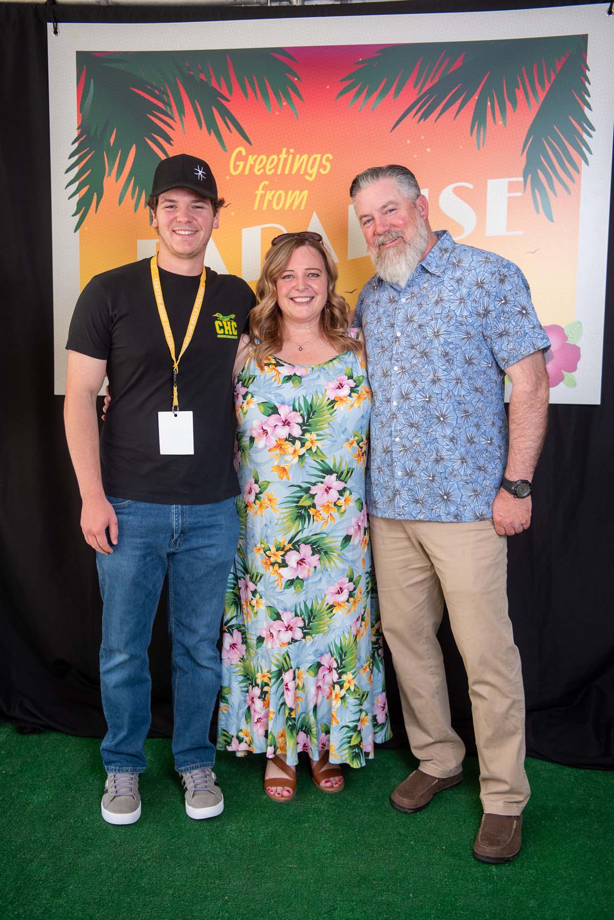 Three people in front of Greetings from Paradise sign