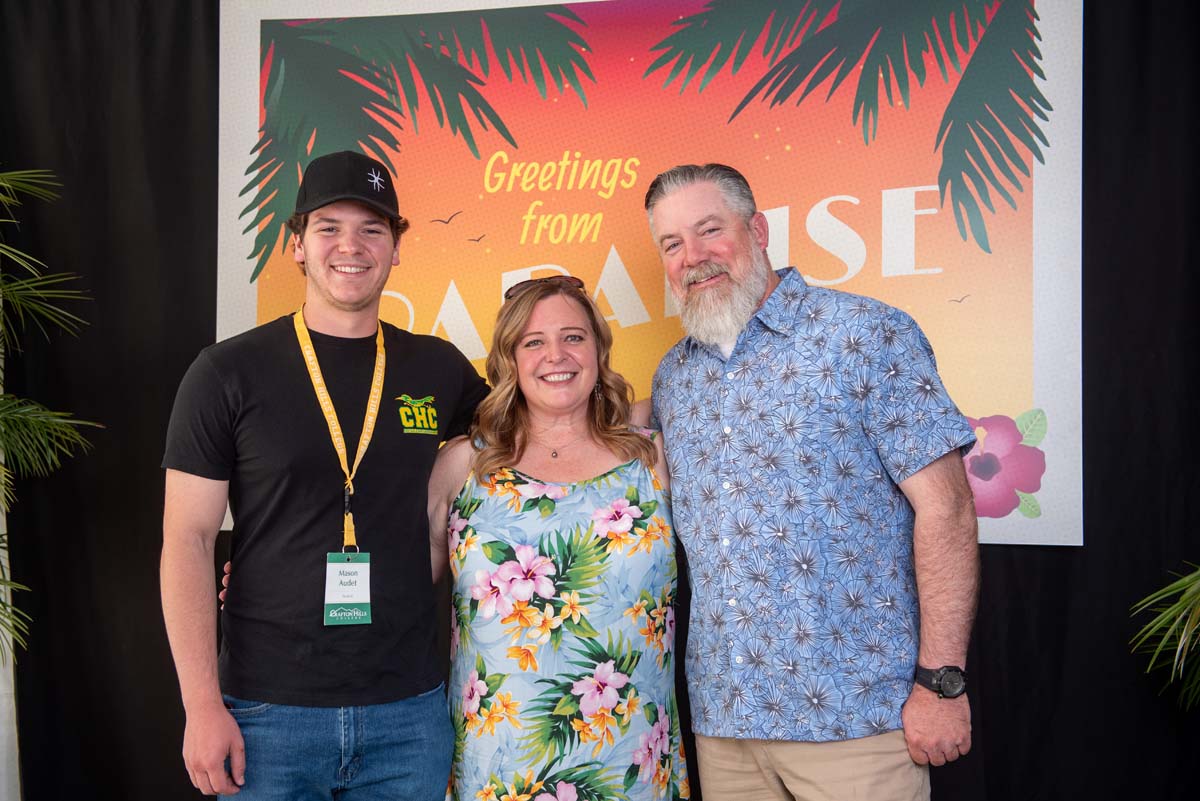 Three people in front of Greetings from Paradise sign