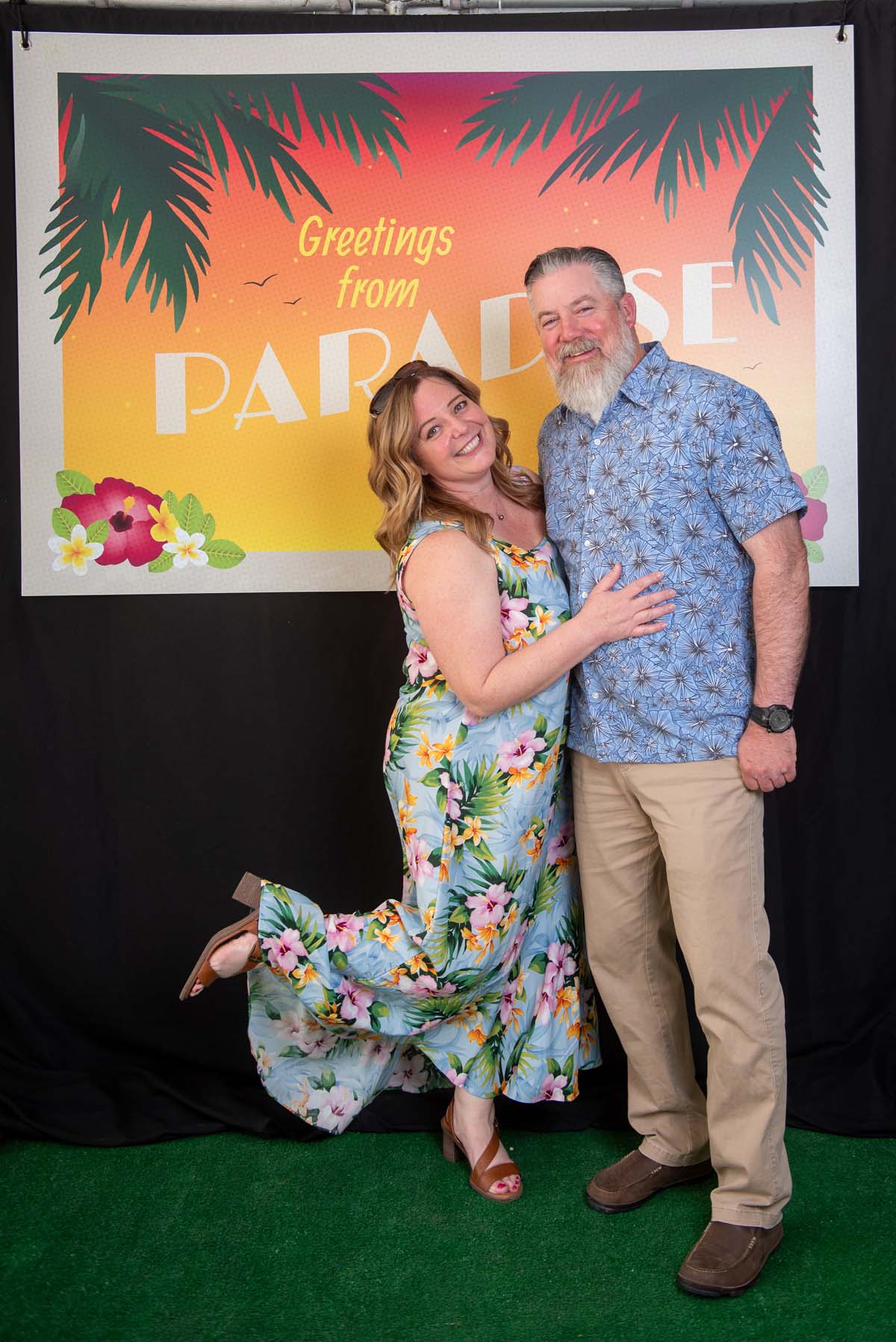 Two people in front of Greetings from Paradise sign