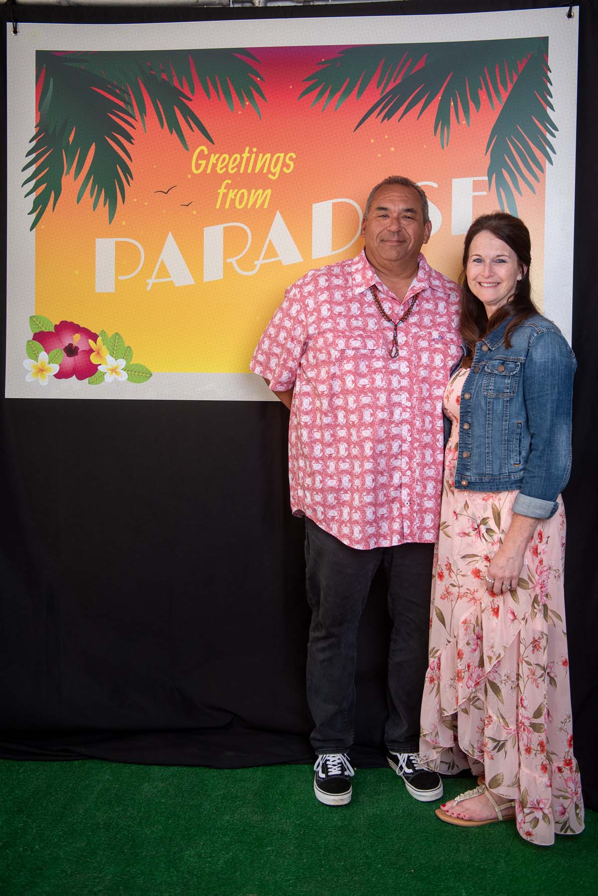 Two people in front of Greetings from Paradise sign