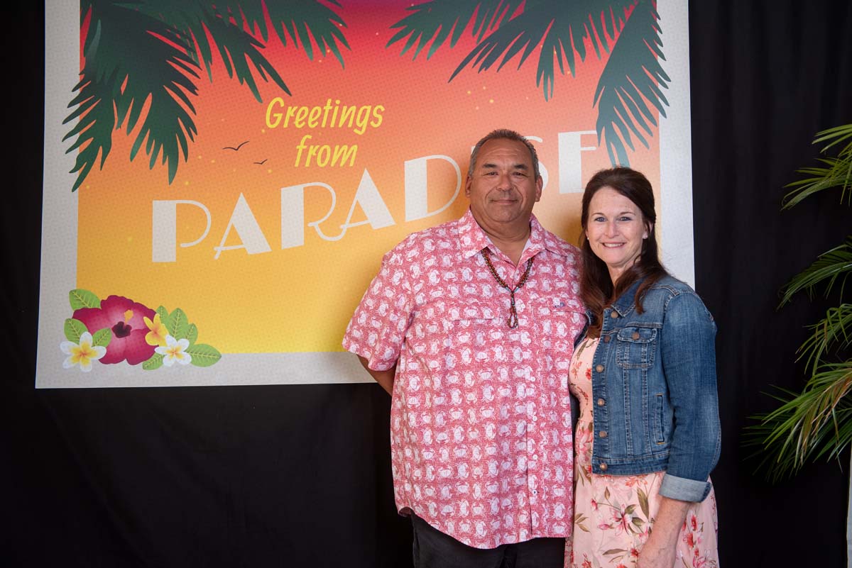 Two people in front of Greetings from Paradise sign