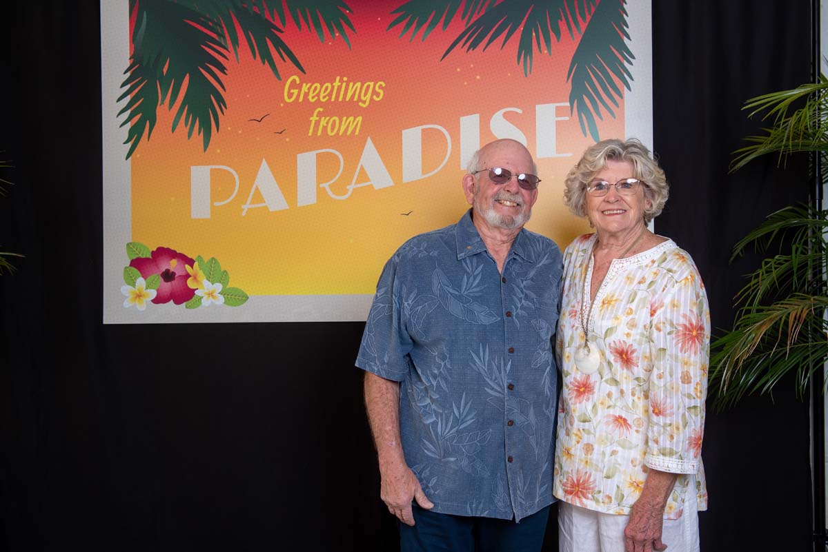 Two people in front of Greetings from Paradise sign
