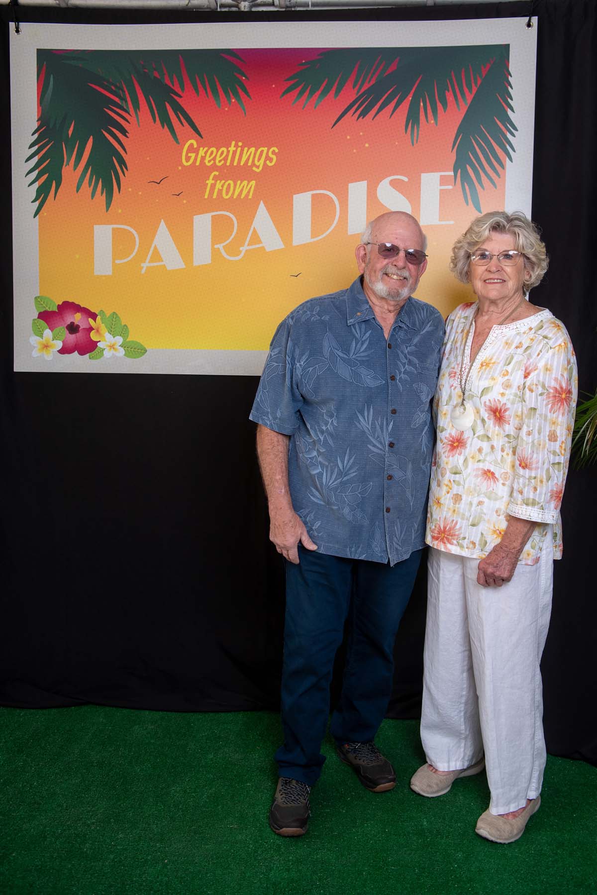 Two people in front of Greetings from Paradise sign