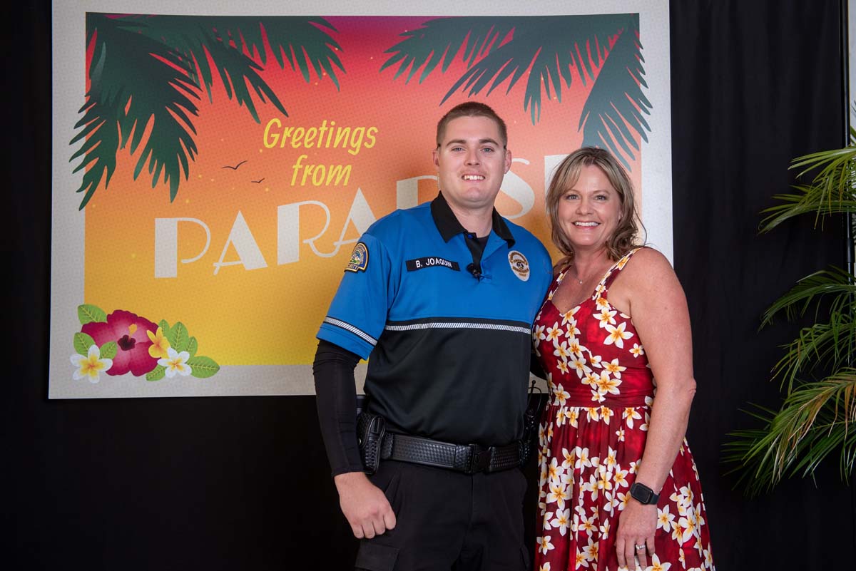 Two people in front of Greetings from Paradise sign