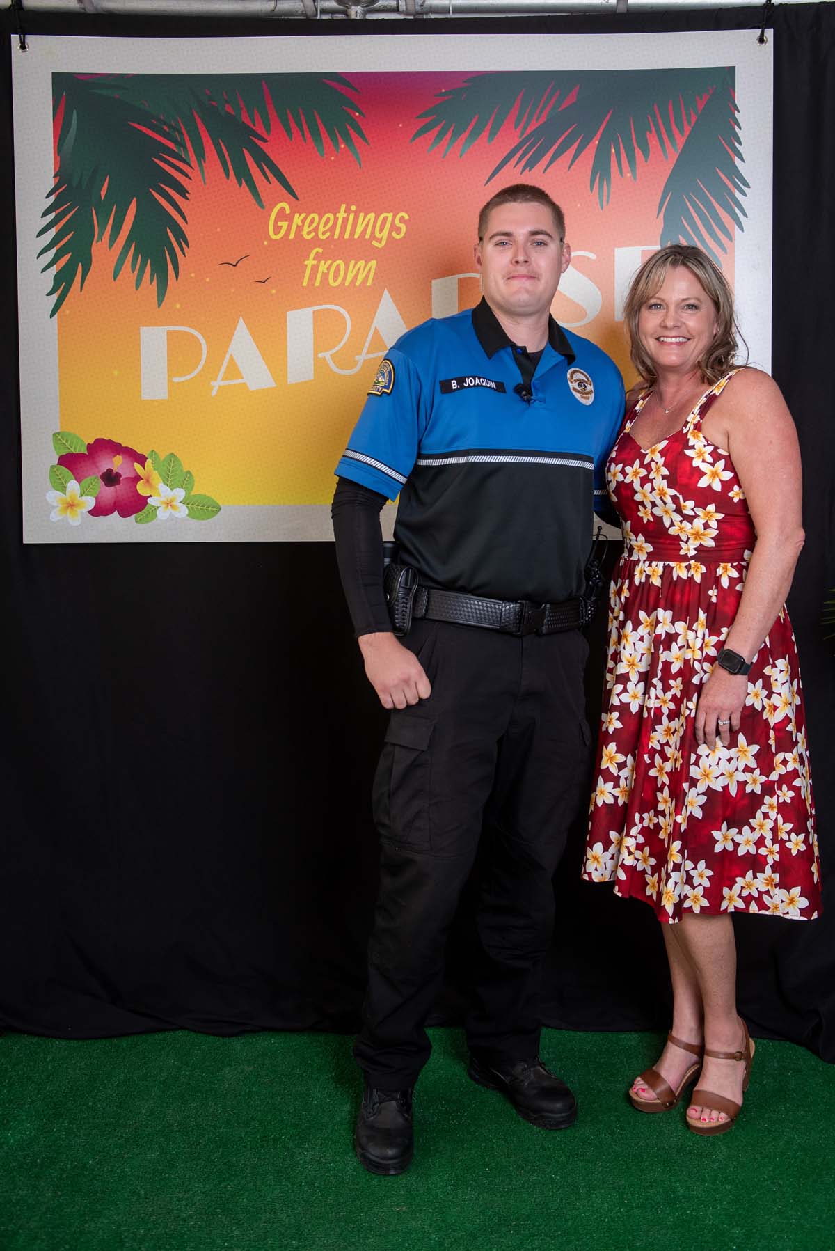 Two people in front of Greetings from Paradise sign
