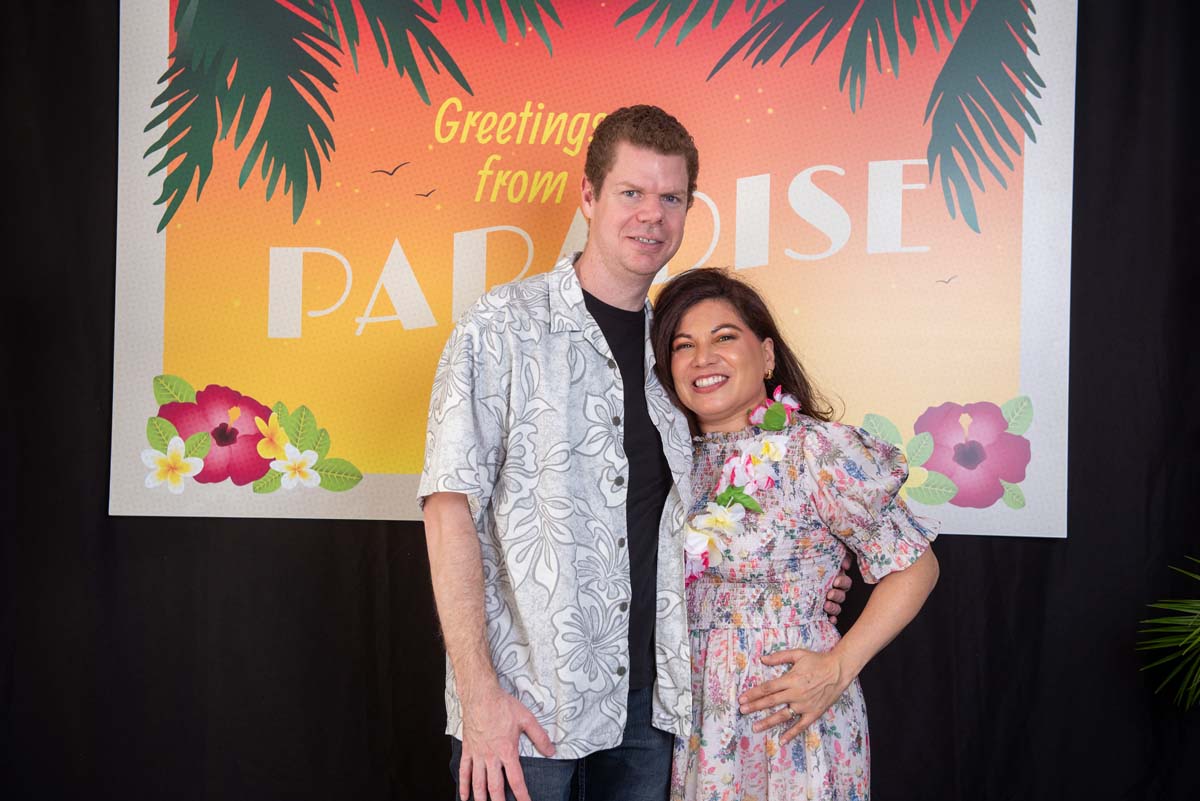 Two people in front of Greetings from Paradise sign