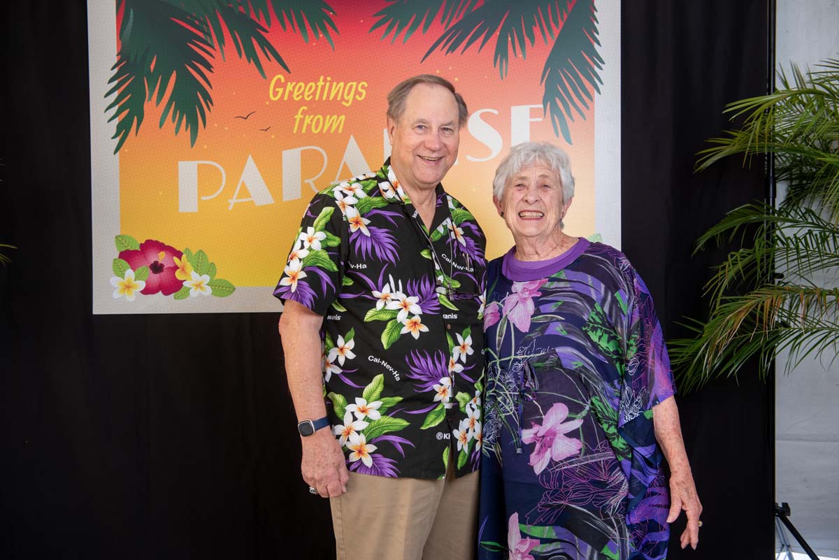 Two people in front of Greetings from Paradise sign