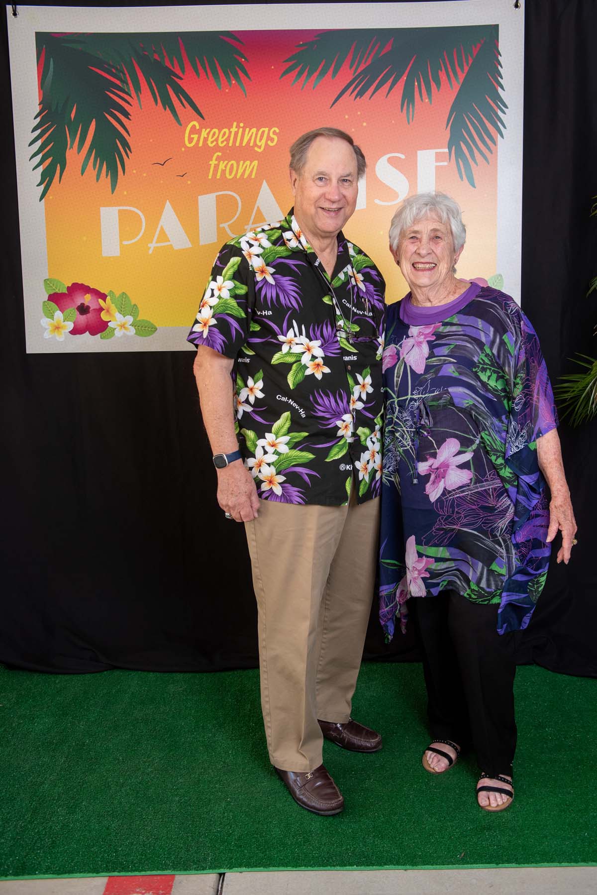 Two people in front of Greetings from Paradise sign