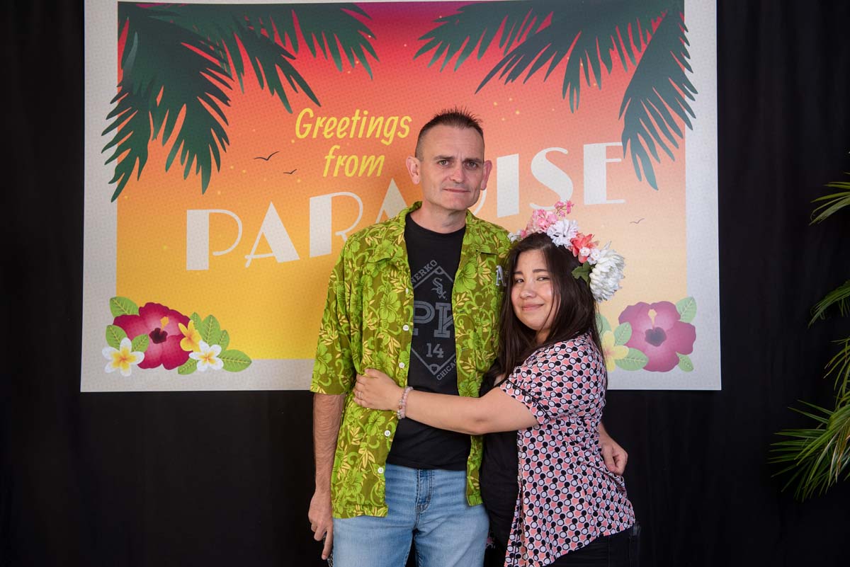 Two people in front of Greetings from Paradise sign