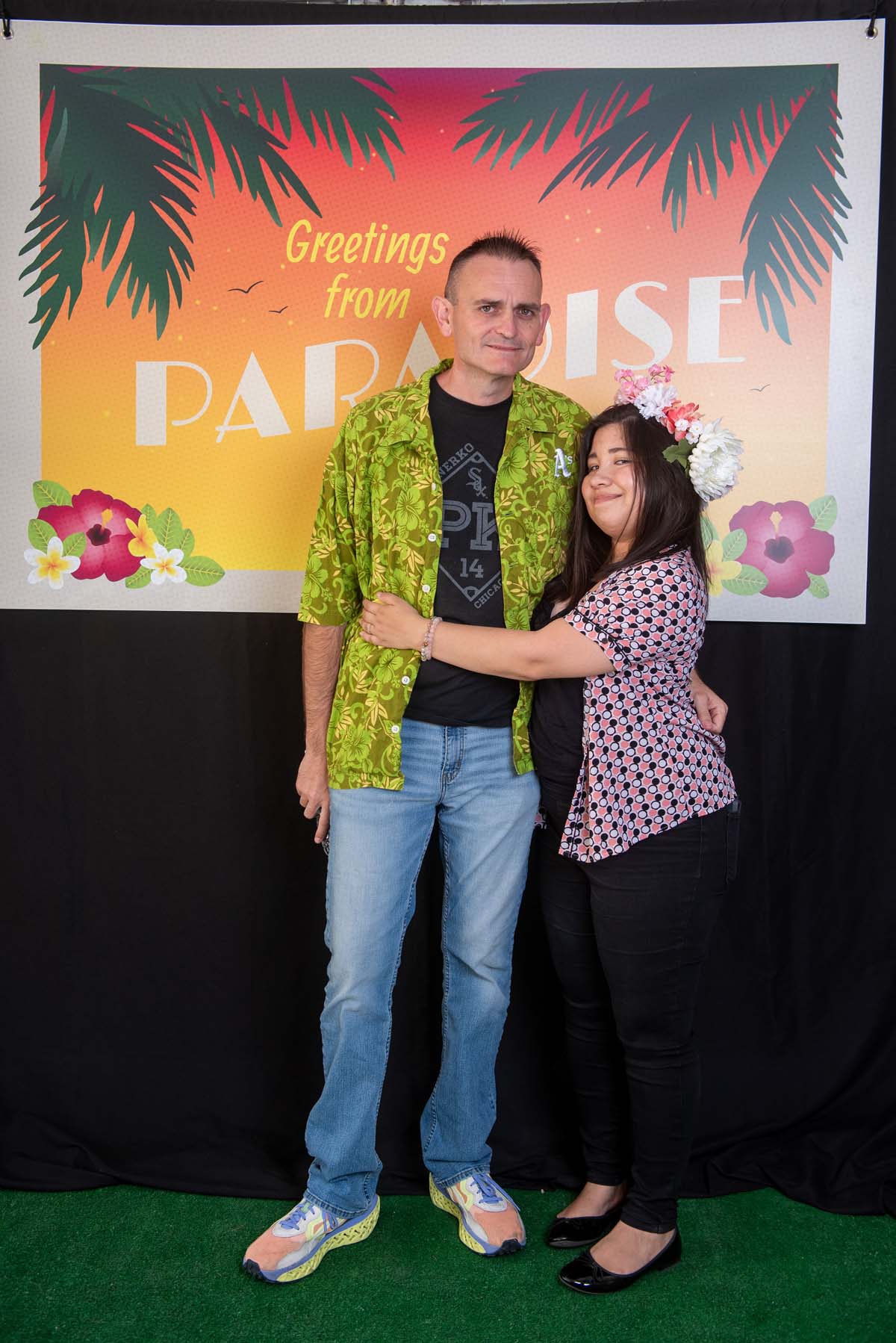 Two people in front of Greetings from Paradise sign