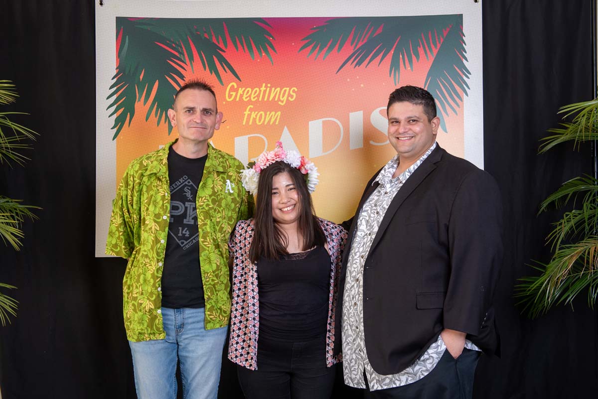 Three people in front of Greetings from Paradise sign
