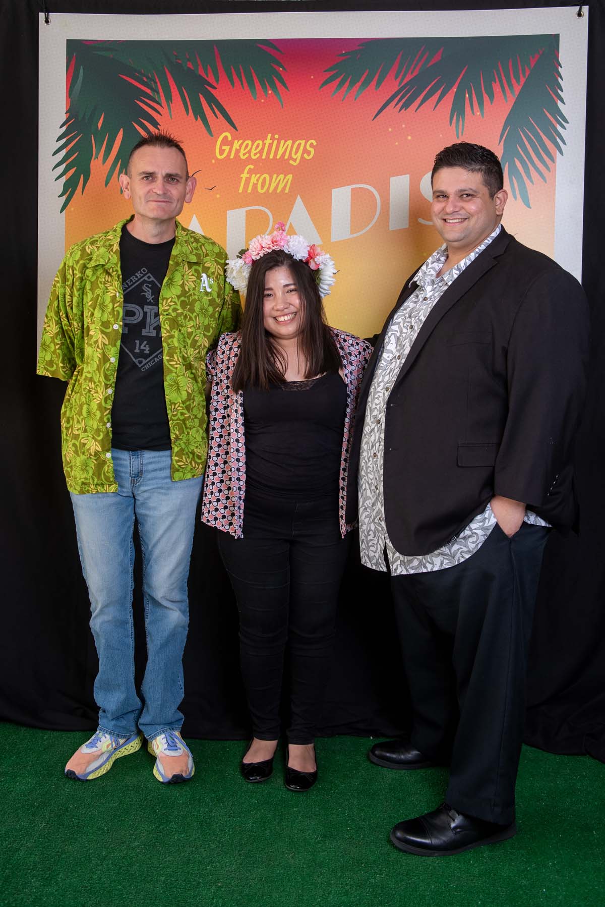 Three people in front of Greetings from Paradise sign
