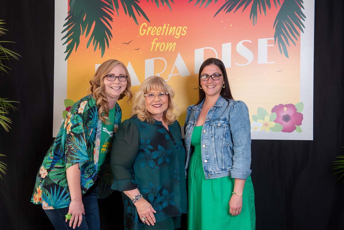 Three women in front of Greetings from Paradise sign