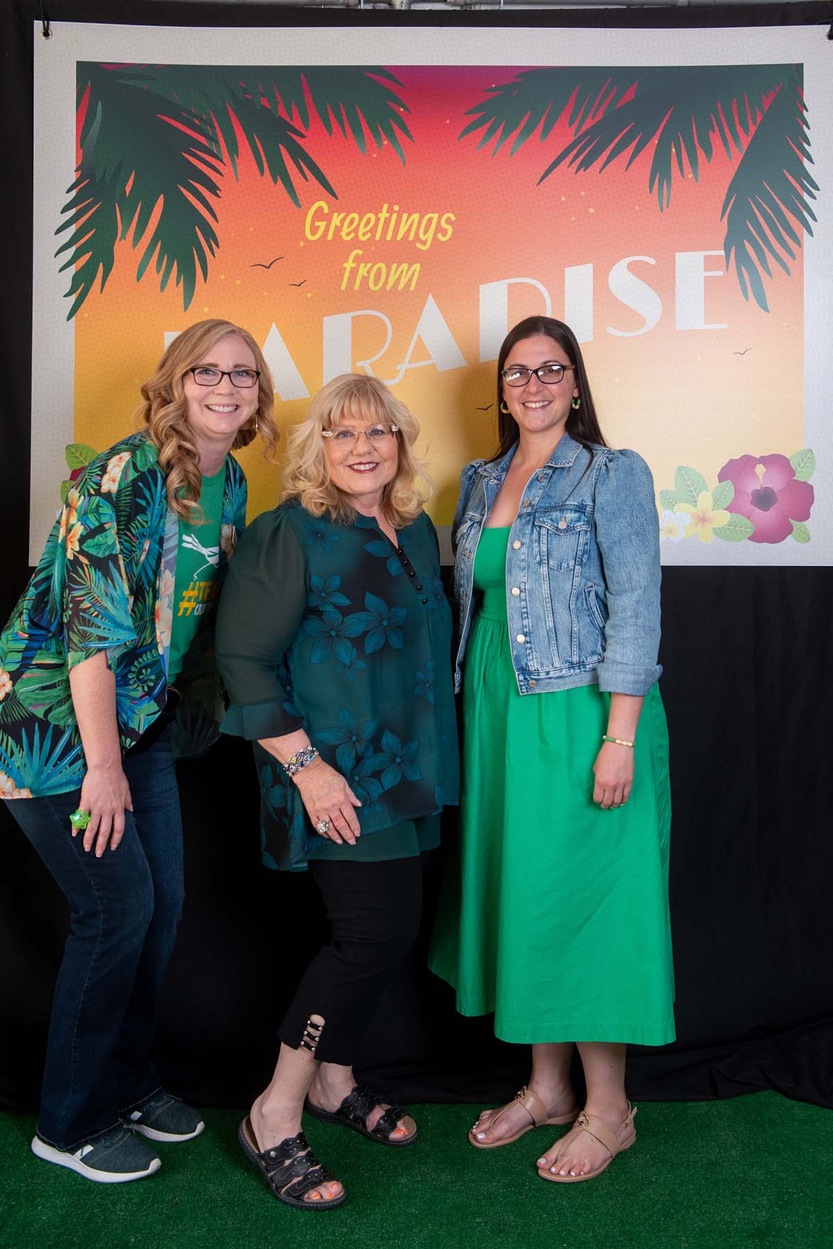 Three women in front of Greetings from Paradise sign