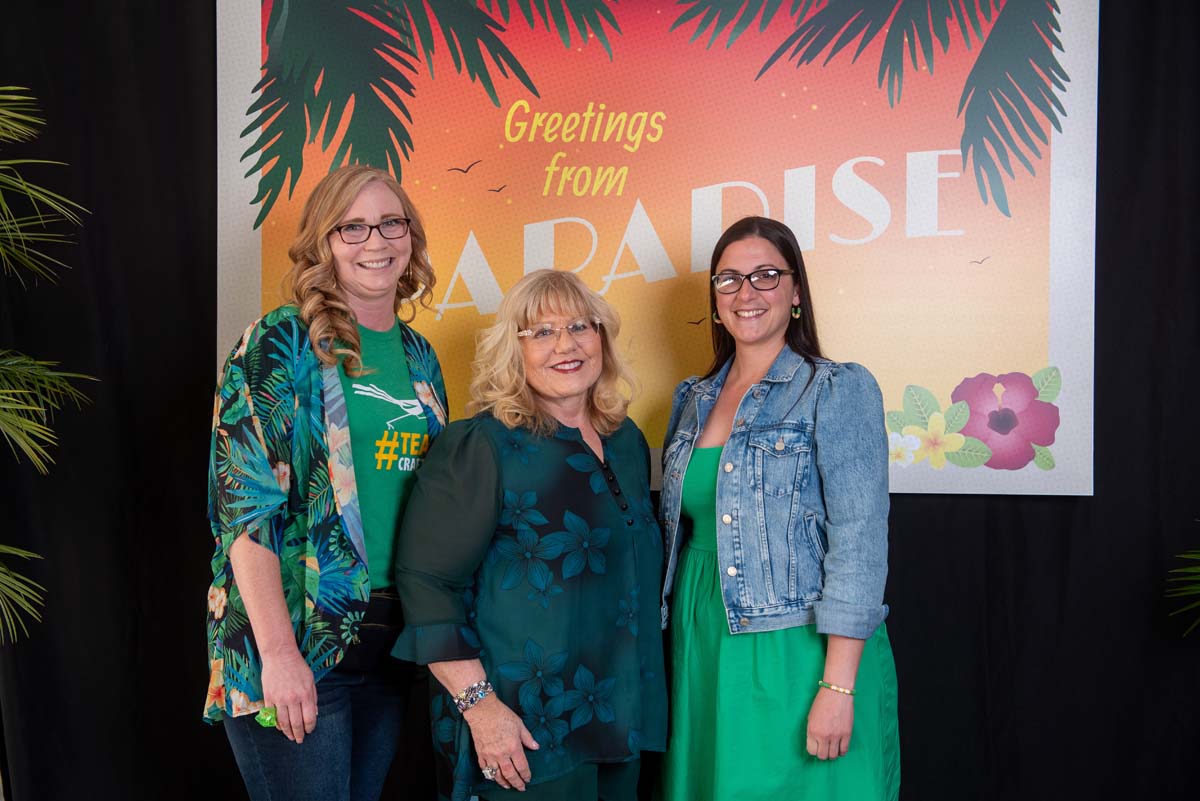 Three women in front of Greetings from Paradise sign
