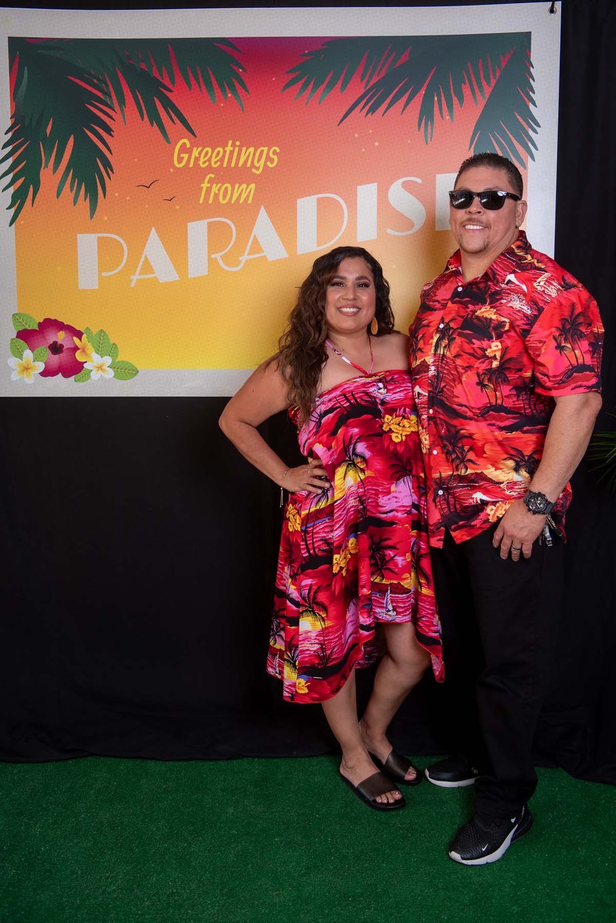 Two people in front of Greetings from Paradise sign