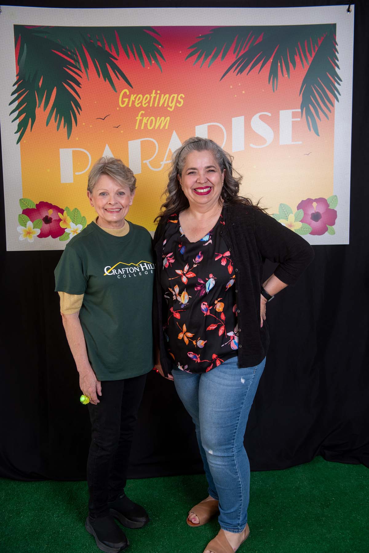 Two people in front of Greetings from Paradise sign