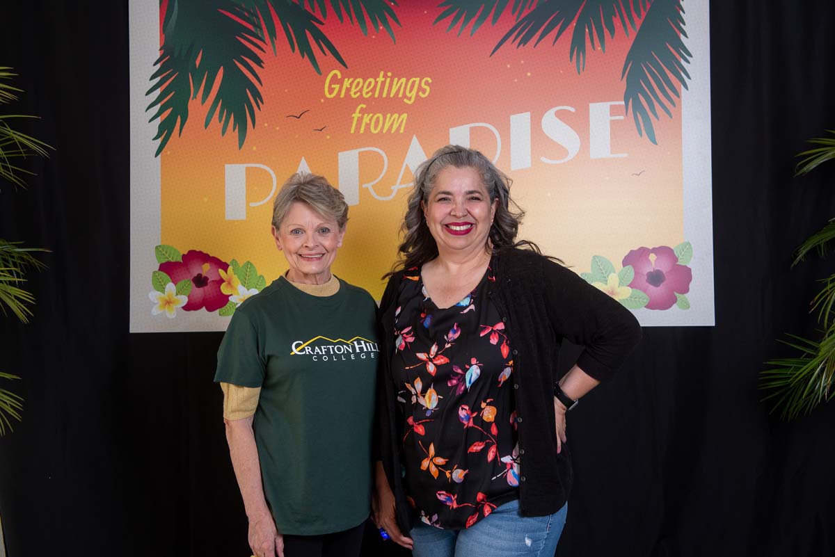 Two people in front of Greetings from Paradise sign