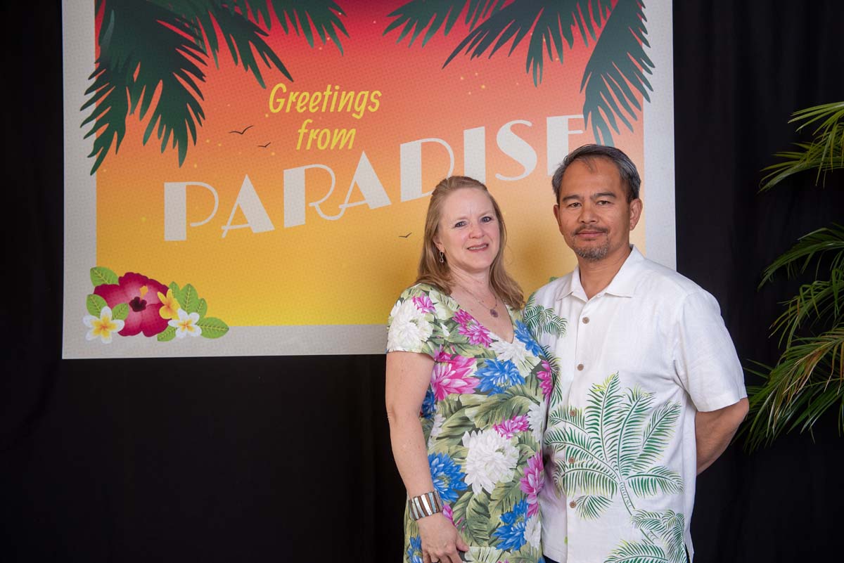 Two people in front of Greetings from Paradise sign