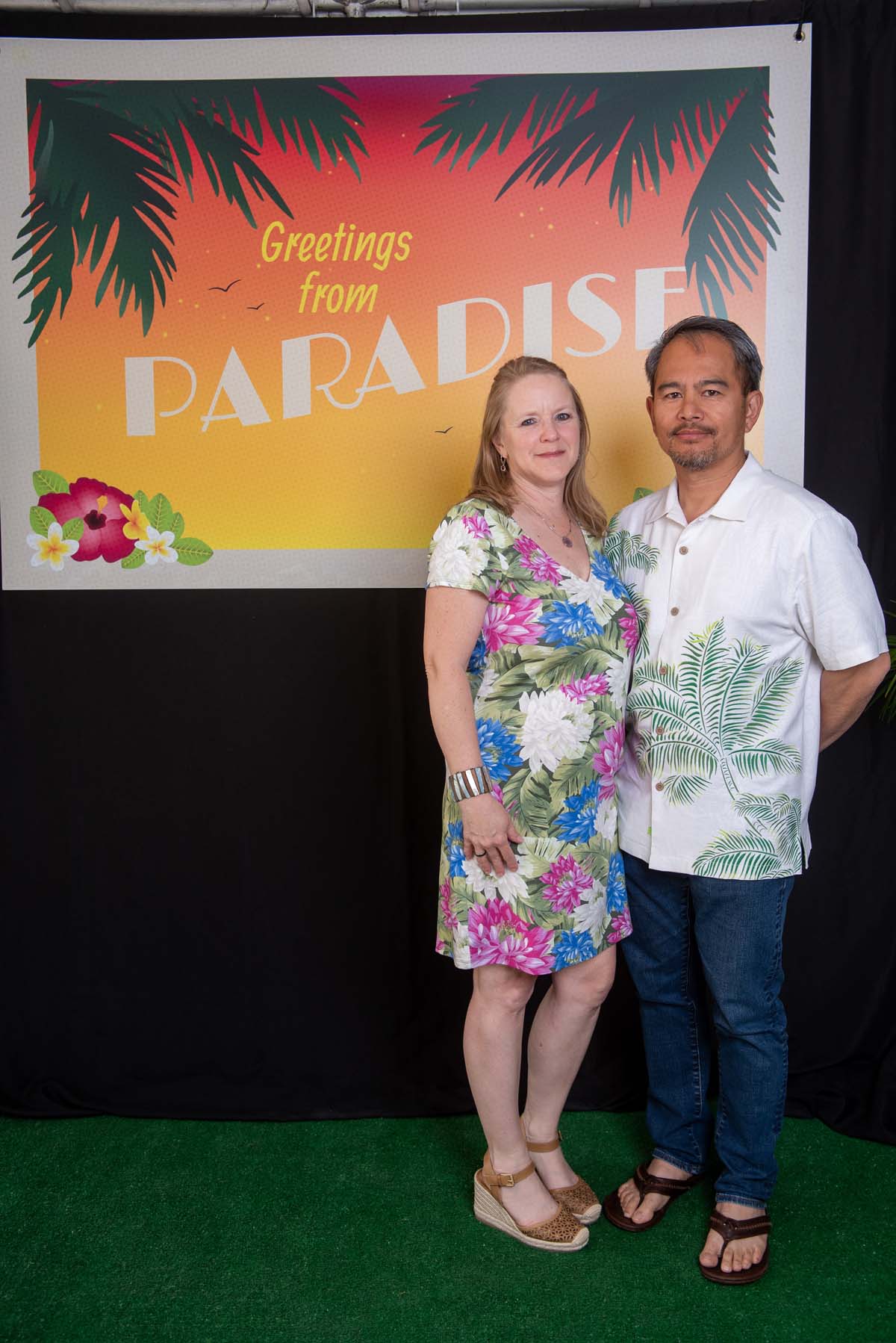 Two people in front of Greetings from Paradise sign
