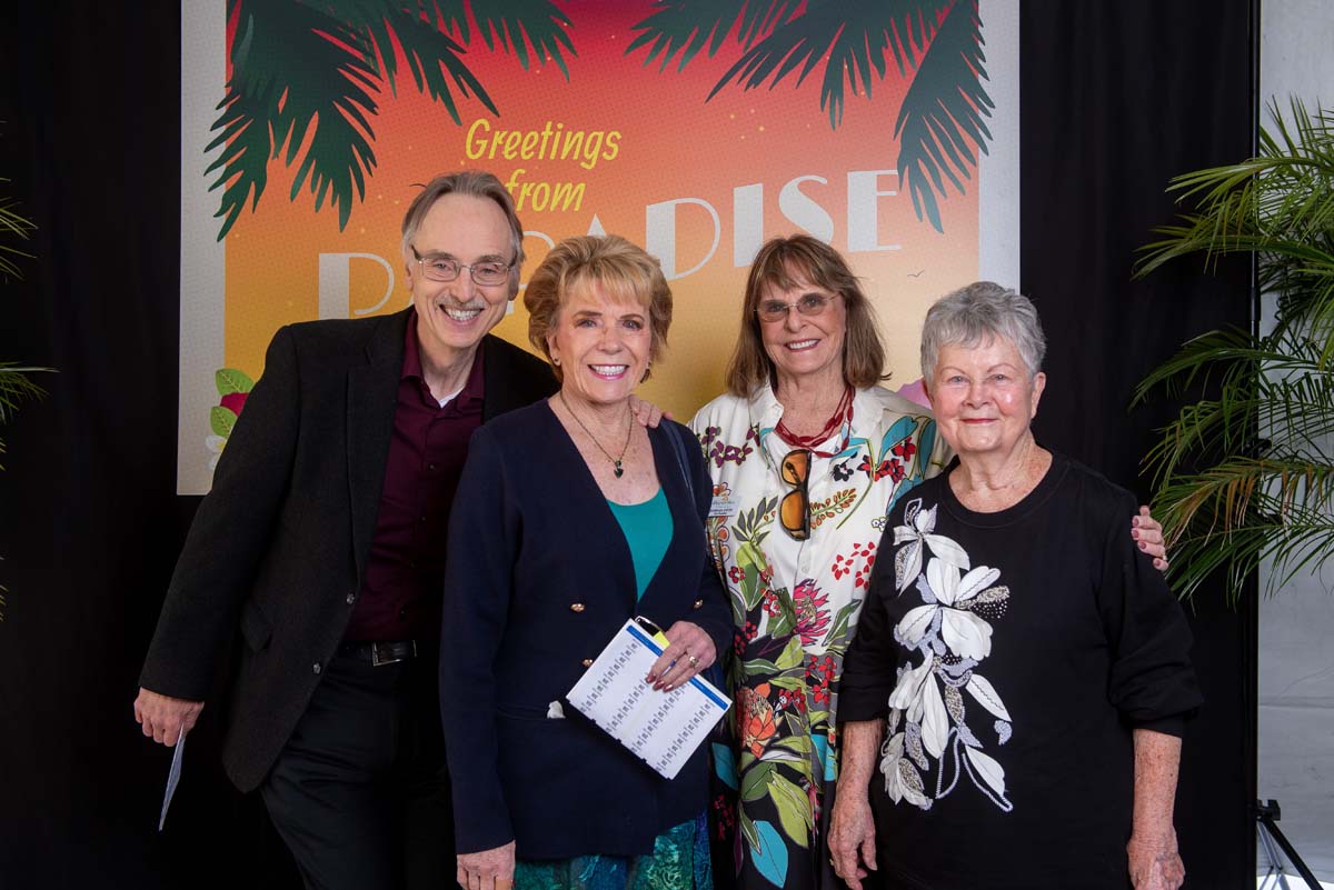 Four people in front of Greetings from Paradise sign