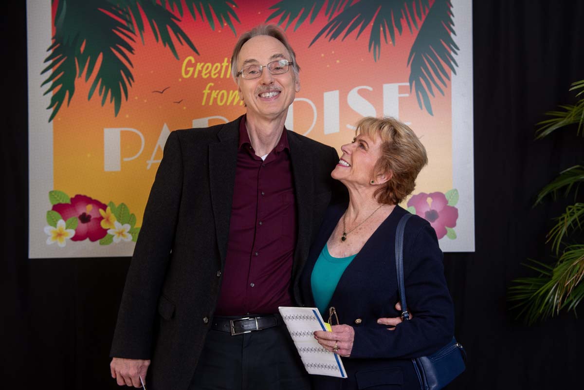 Two people in front of Greetings from Paradise sign