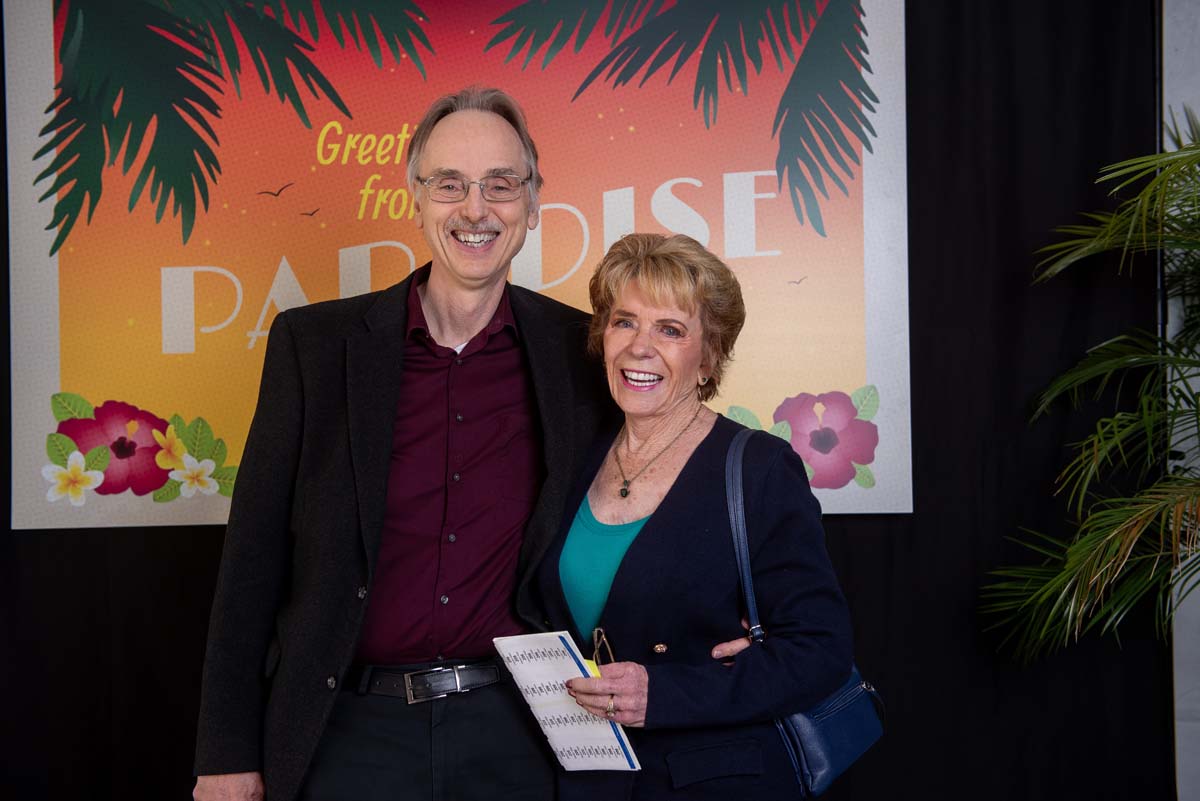 Two people in front of Greetings from Paradise sign