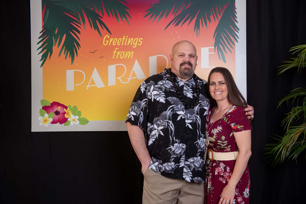 Two people in front of Greetings from Paradise sign