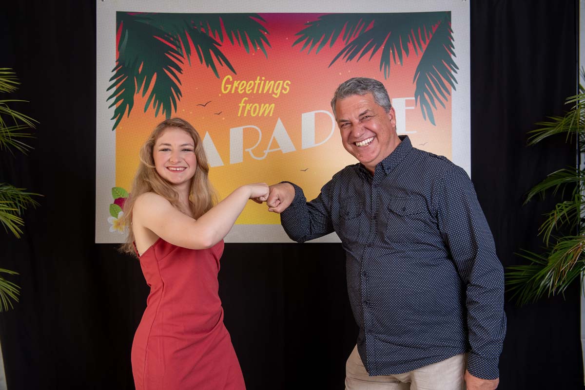 Two people fistbumping in front of Greetings from Paradise sign