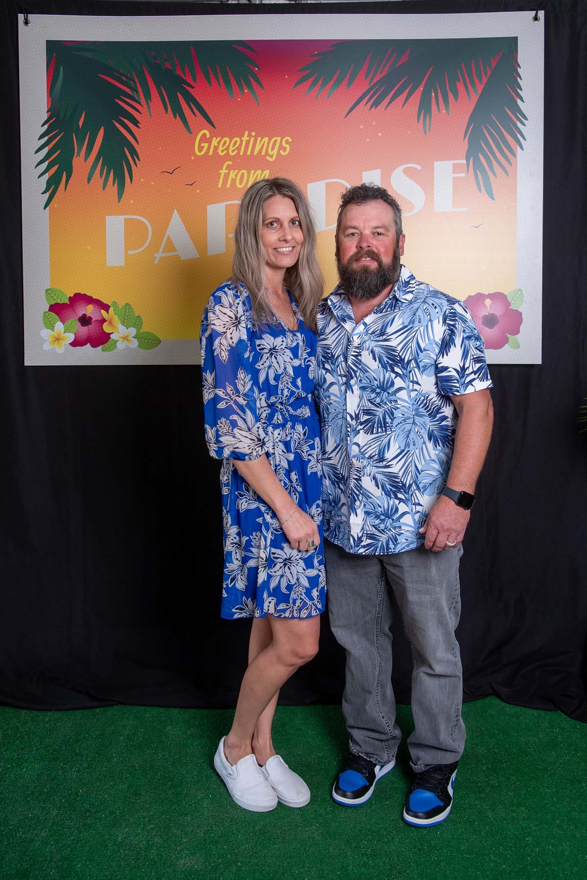 Two people in front of Greetings from Paradise sign