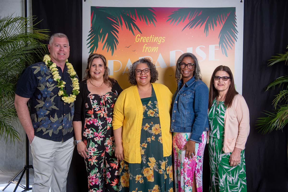 Five people in front of Greetings from Paradise sign