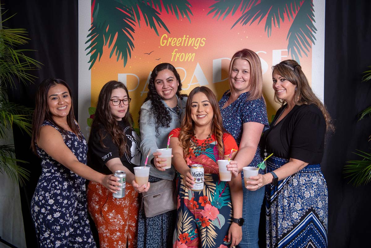 Six women in front of Greetings from Paradise sign