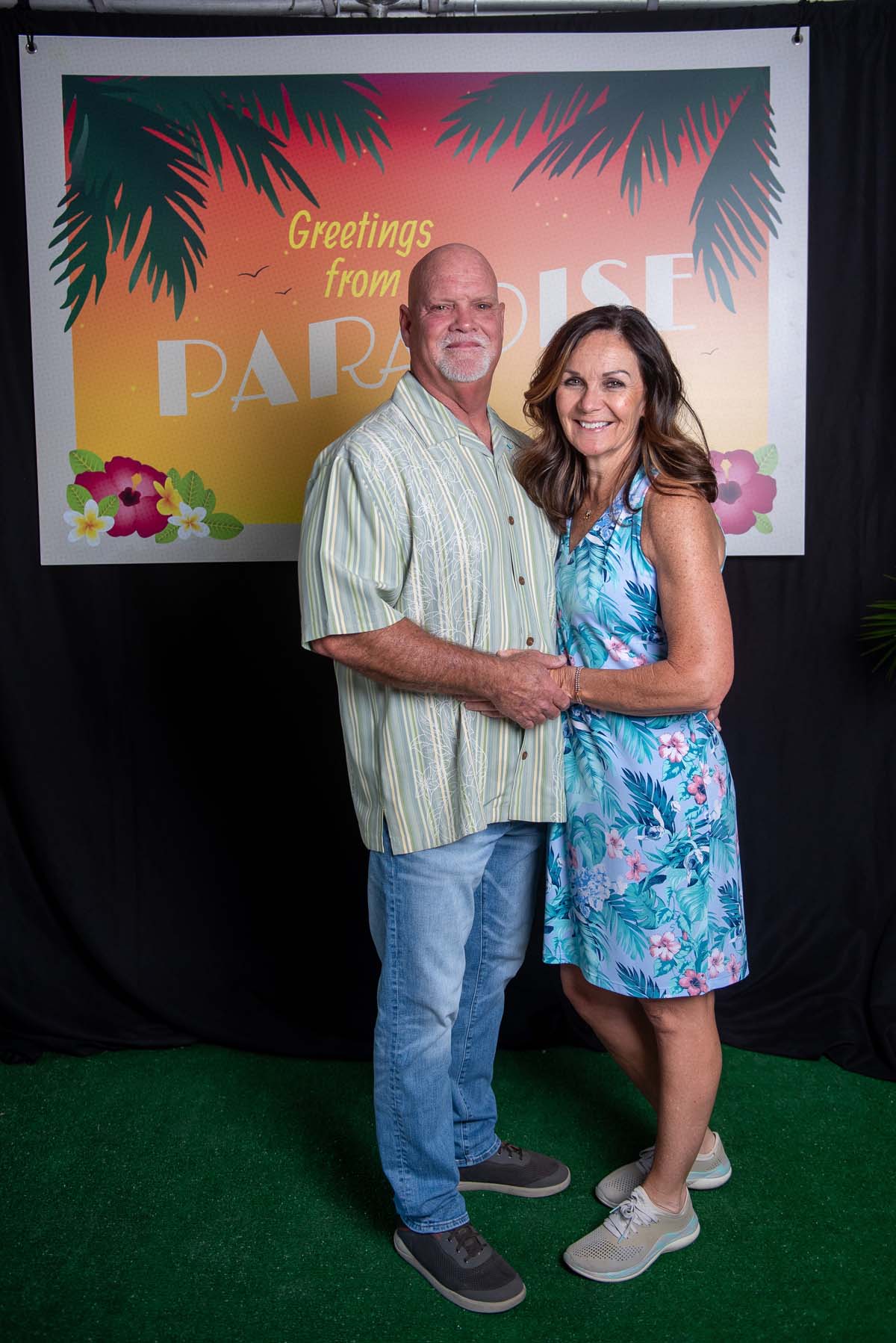 Two people in front of Greetings from Paradise sign