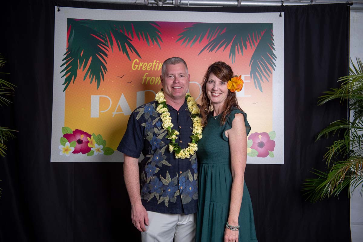 Two people in front of Greetings from Paradise sign