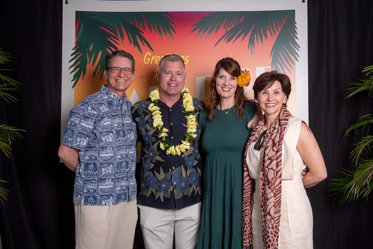 Four people in front of Greetings from Paradise sign