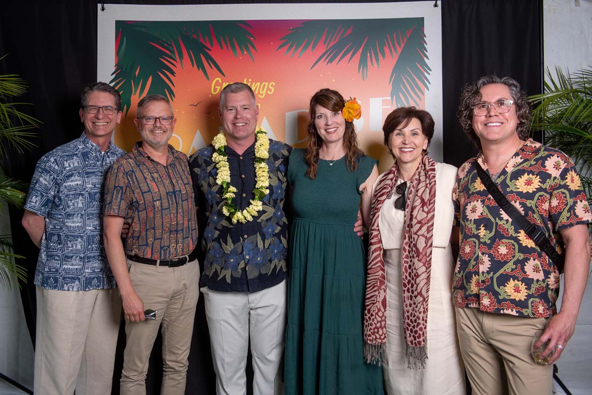 Six people in front of Greetings from Paradise sign