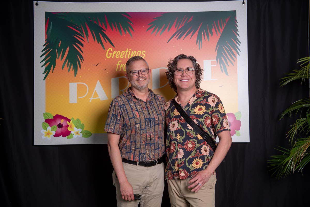 Two men in front of Greetings from Paradise sign