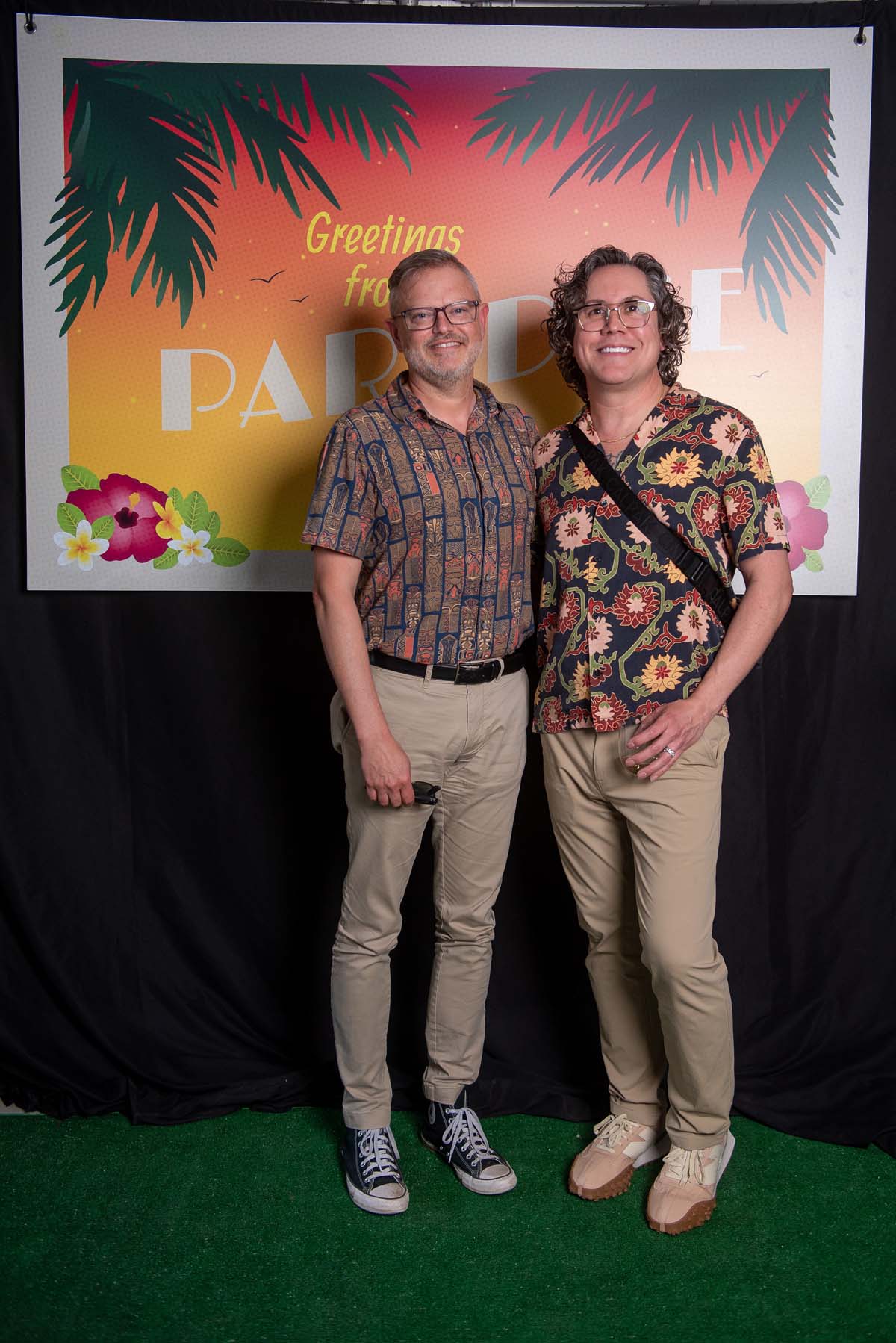 Two men in front of Greetings from Paradise sign