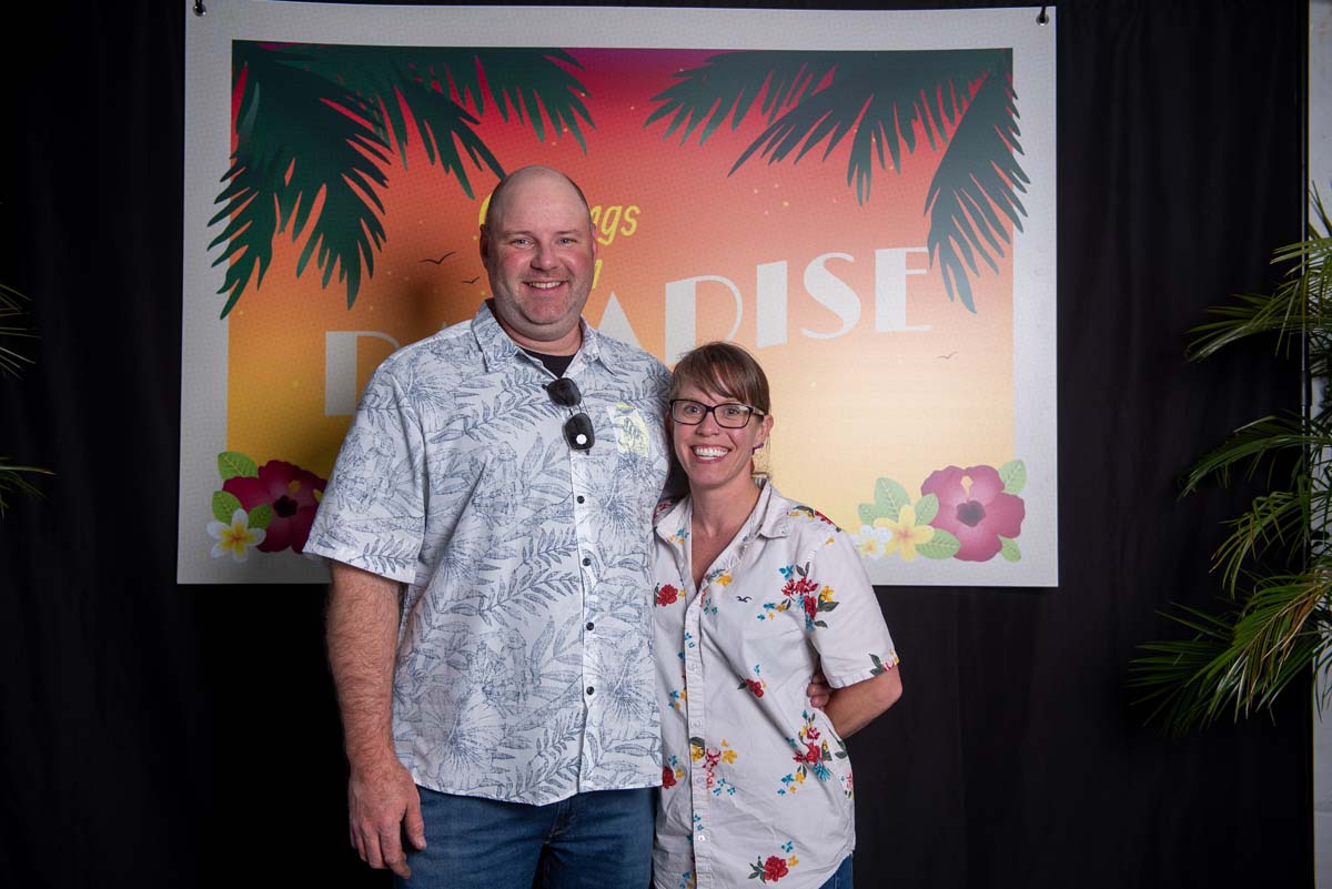 Two people in front of Greetings from Paradise sign