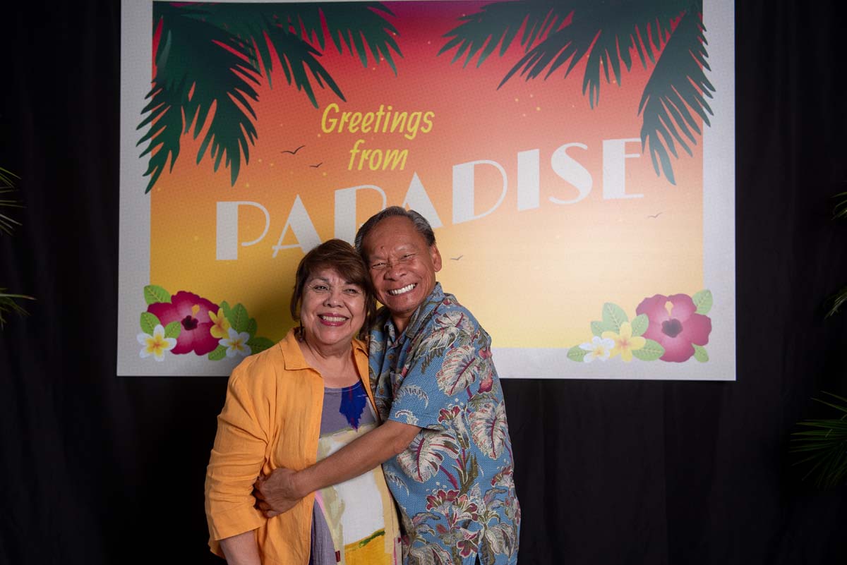 Two people in front of Greetings from Paradise sign
