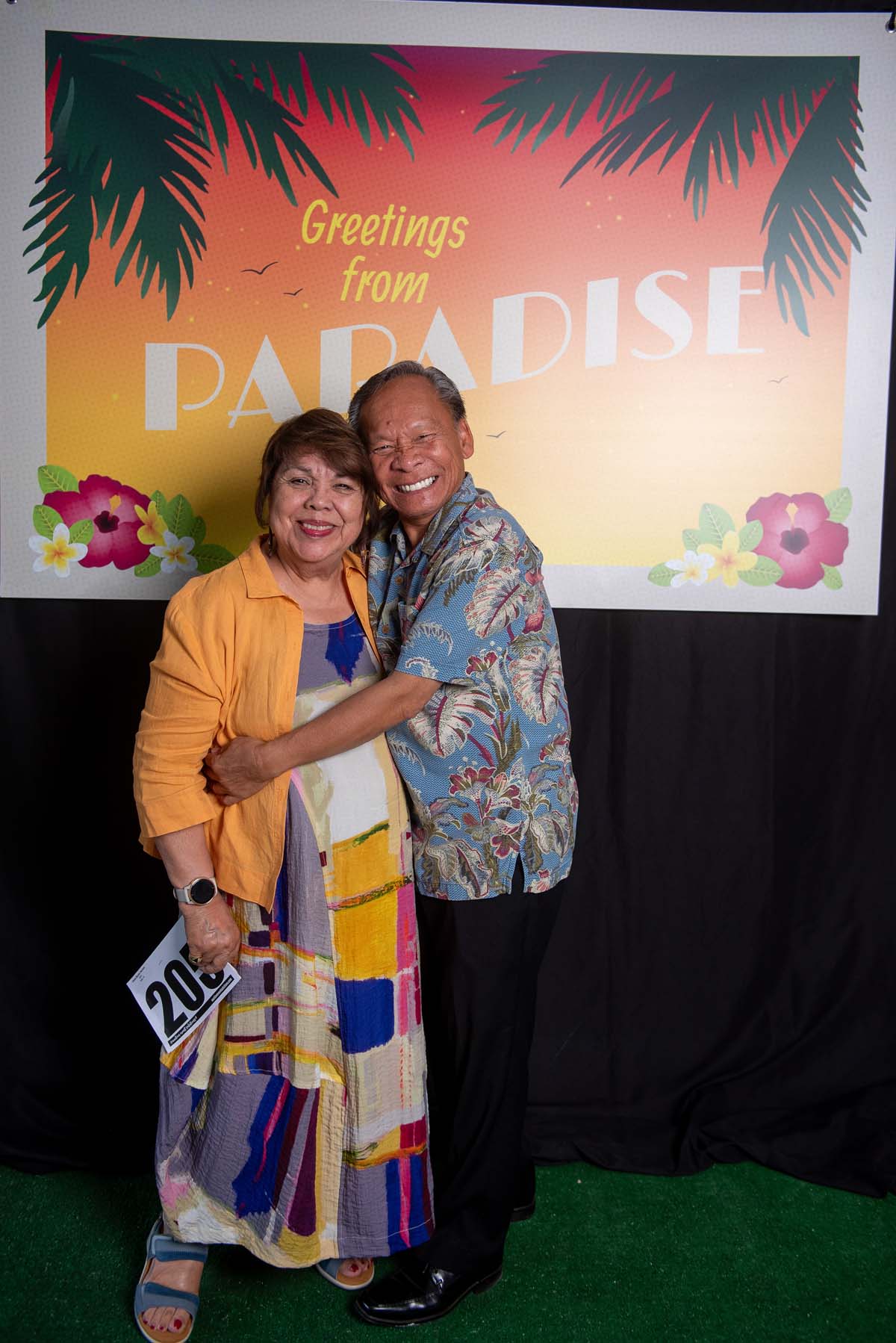 Two people in front of Greetings from Paradise sign