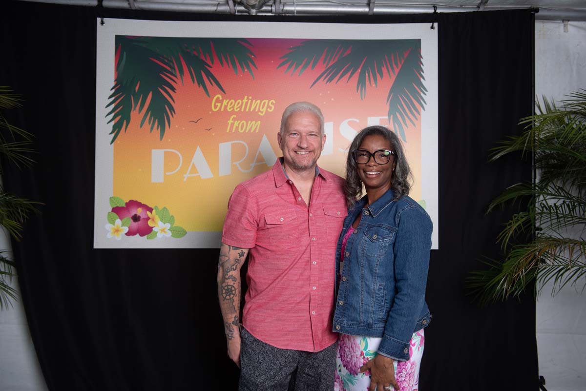 Two people in front of Greetings from Paradise sign