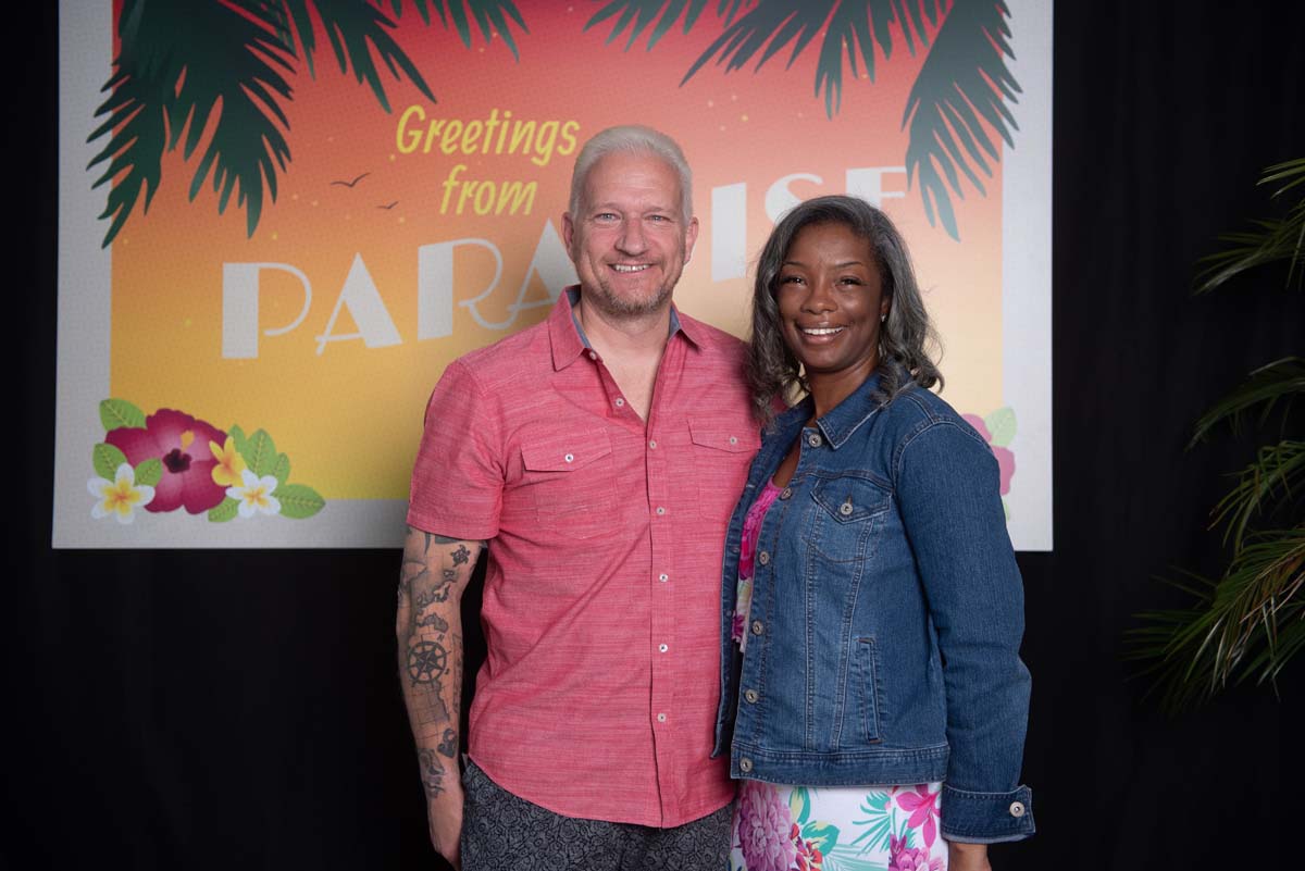 Two people in front of Greetings from Paradise sign