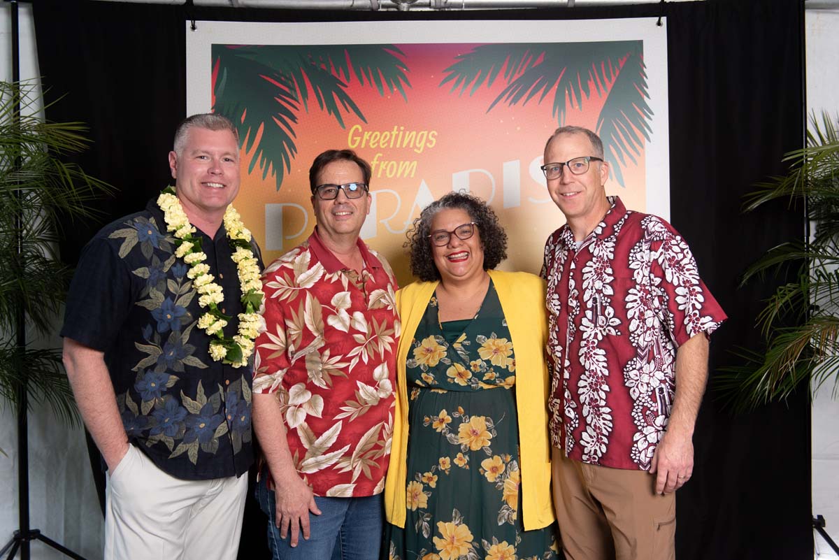 Four people in front of Greetings from Paradise sign