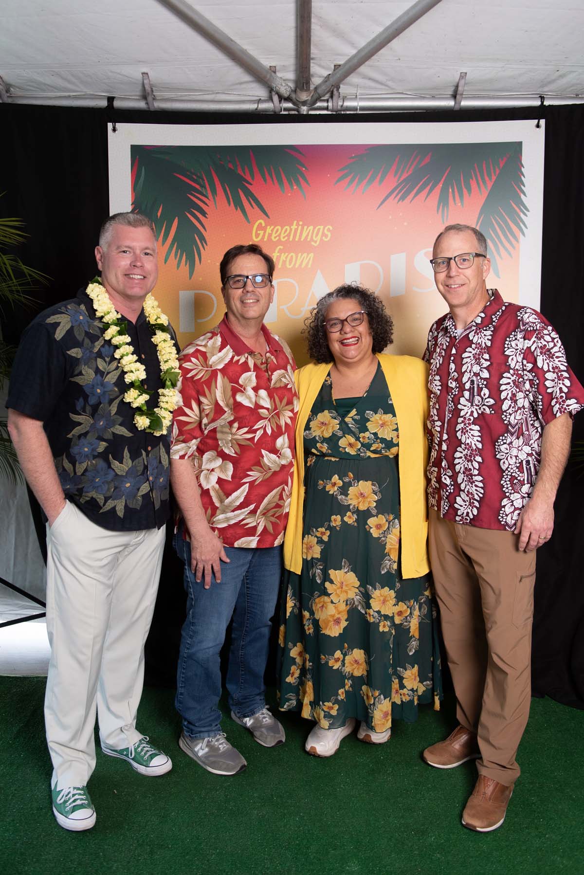 Four people in front of Greetings from Paradise sign