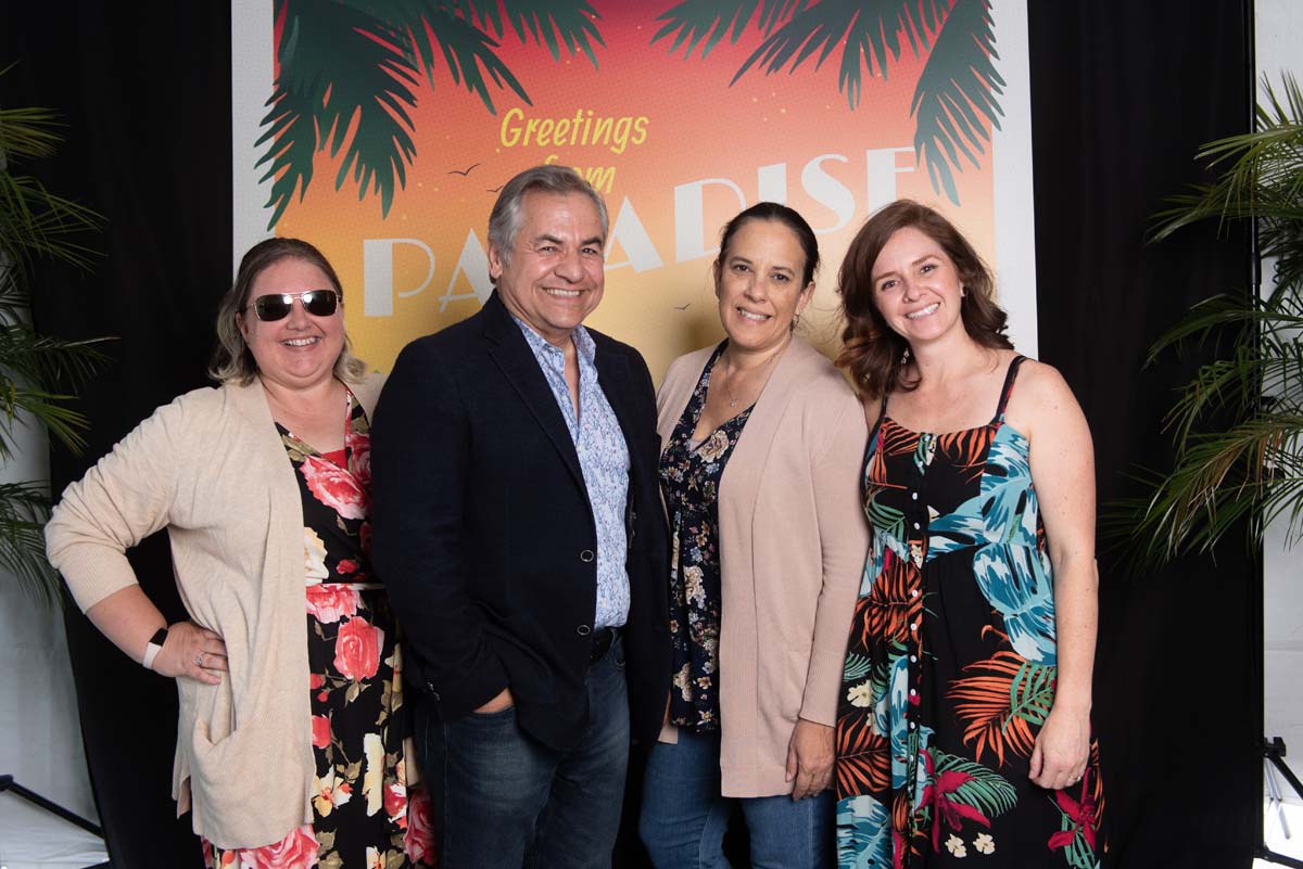 Four people in front of Greetings from Paradise sign