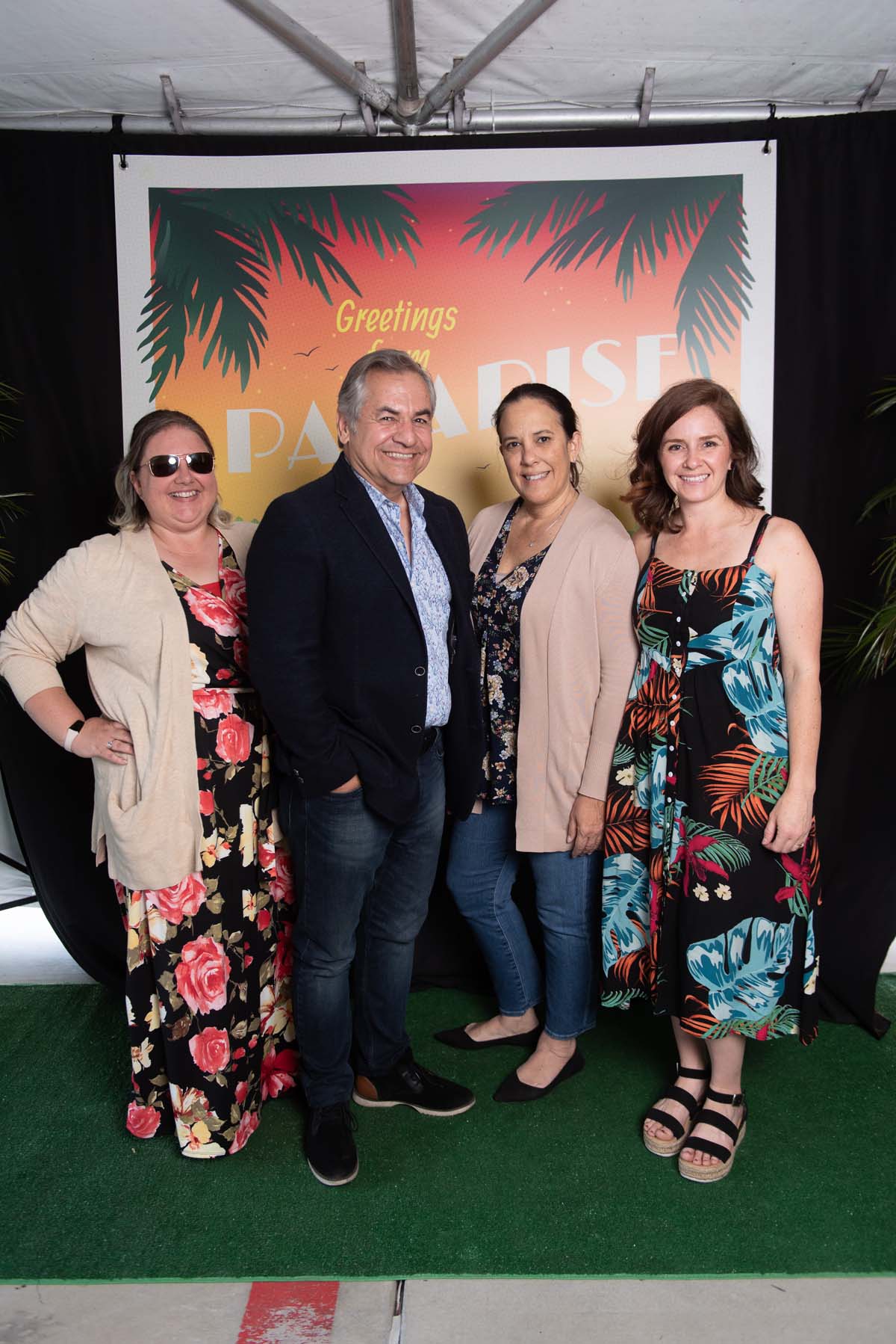 Four people in front of Greetings from Paradise sign