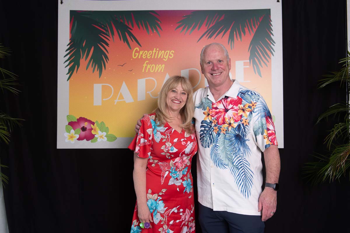 Two people in front of Greetings from Paradise sign