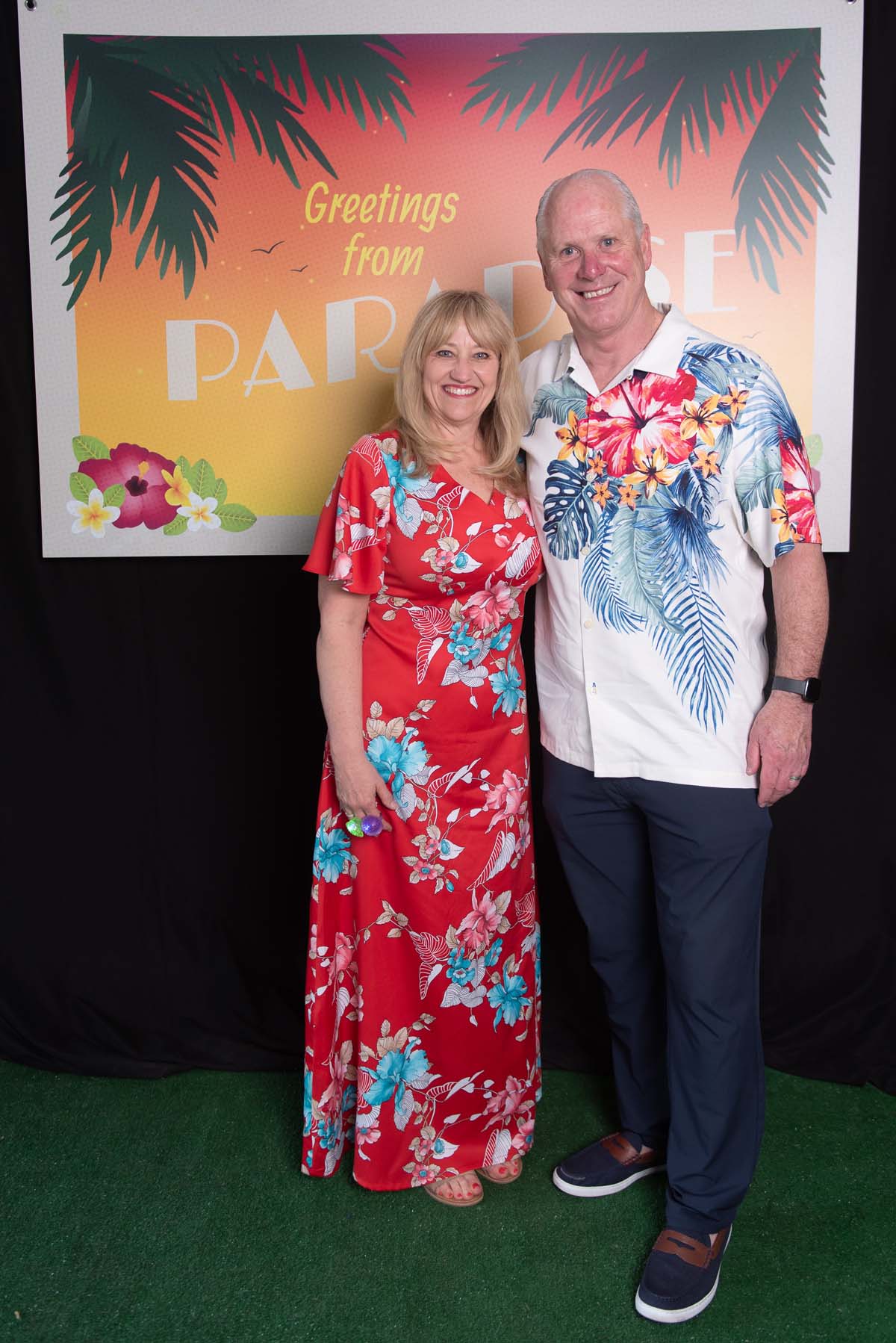 Two people in front of Greetings from Paradise sign